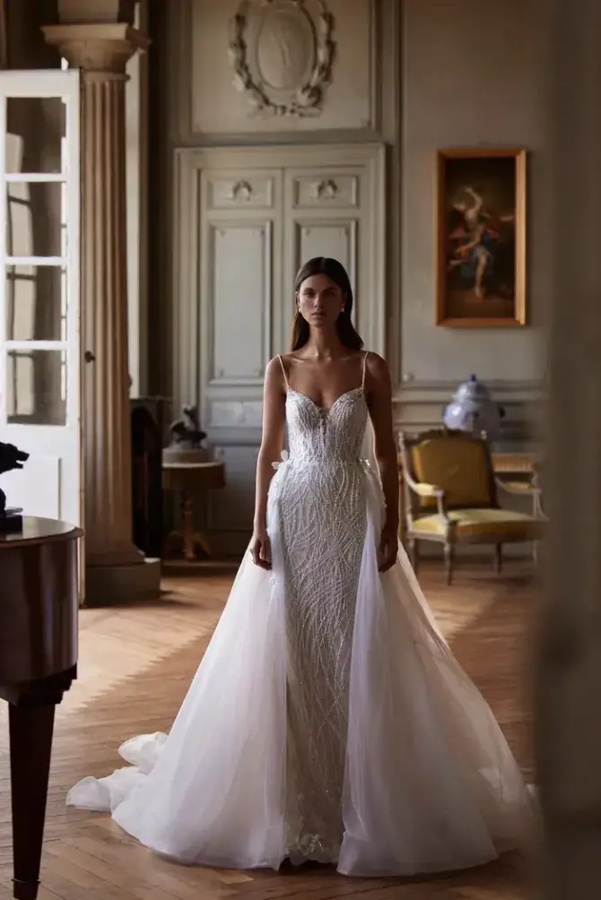 model is wearing a sleeveless wedding dress with an overskirt