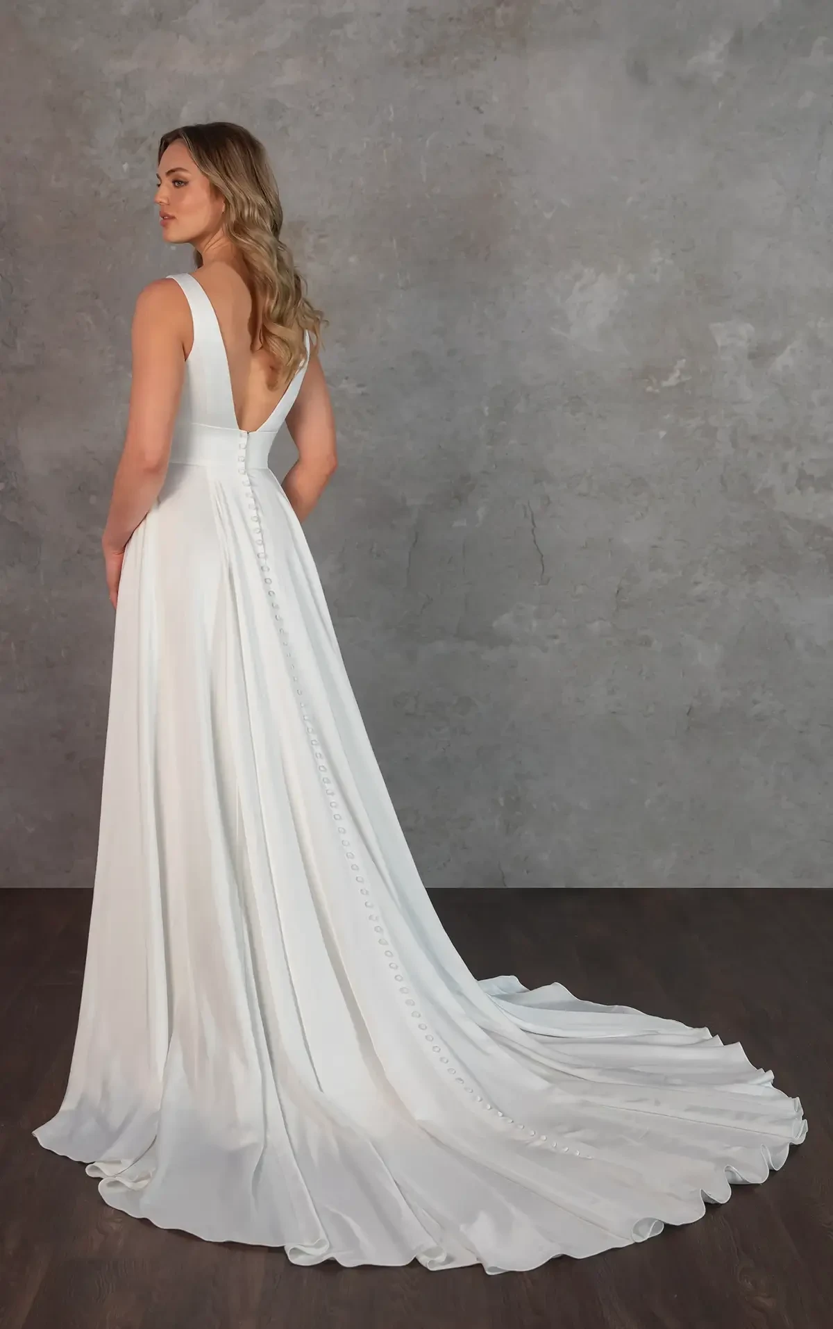 Model is wearing a sleek satin A-line wedding gown with a deep V-neckline, sculpted bodice, V-back, and flowing pleated skirt.