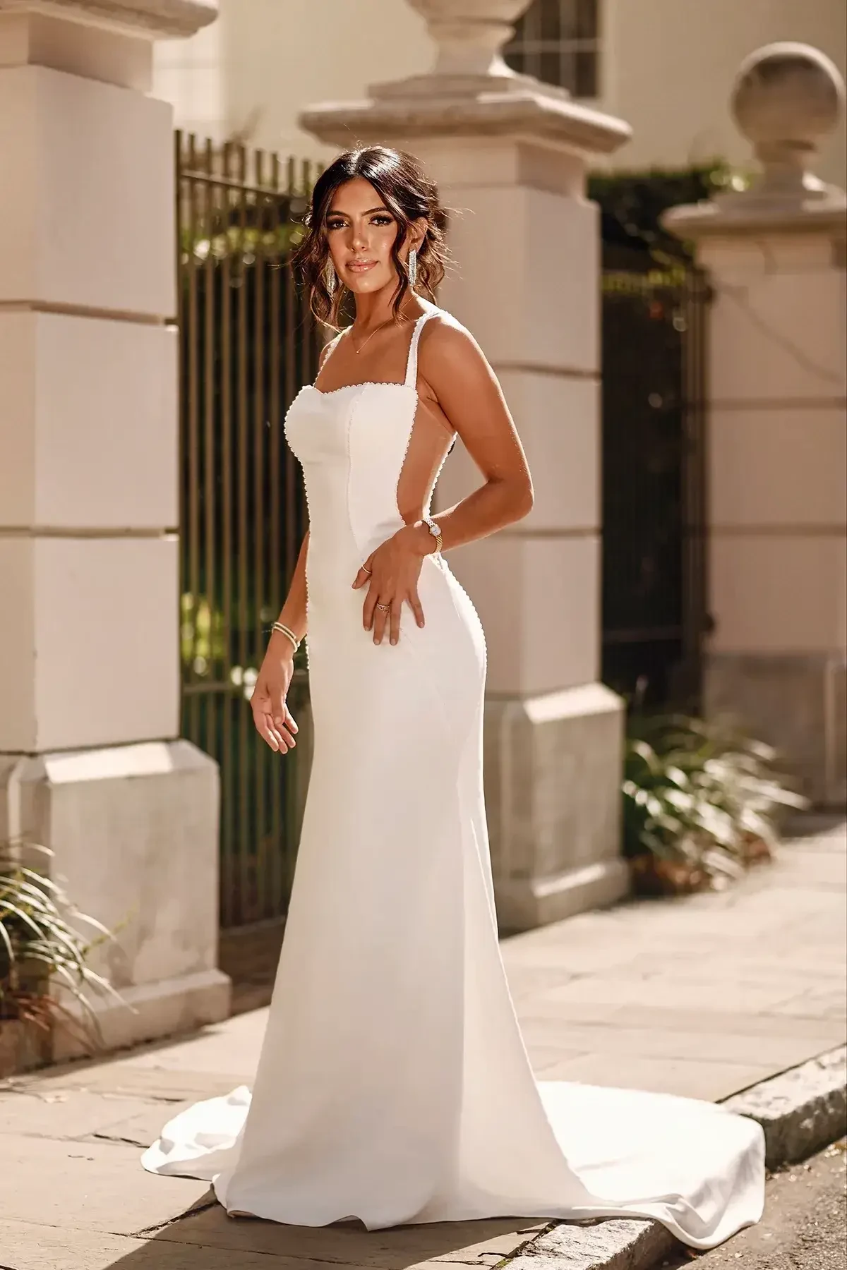 Model is wearing a crepe sheath gown with a square neckline, sheer side cutouts, pearl-beaded seams, and a sleek column silhouette.