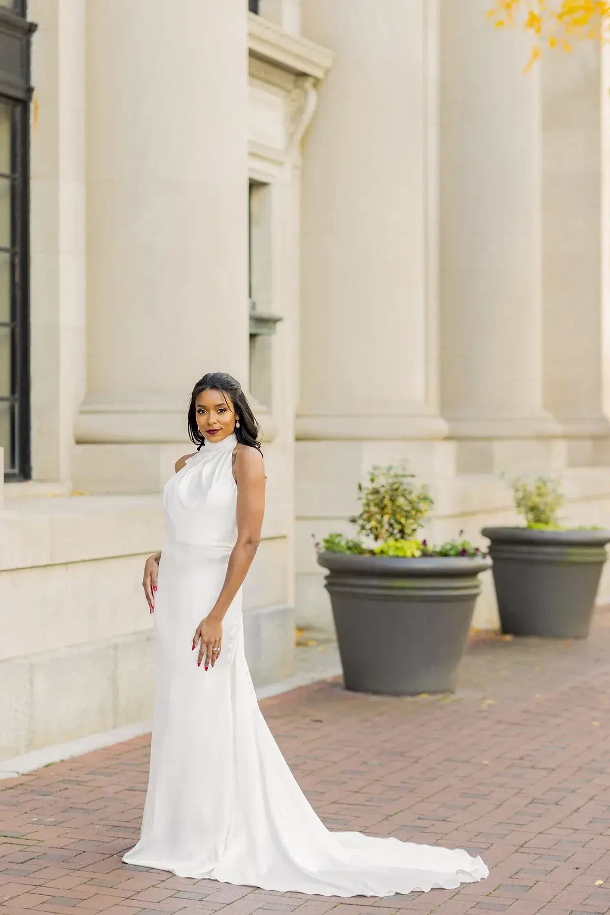 Sleek halter column gown with a draped neckline, open back, pearl button detail, and sweeping train.