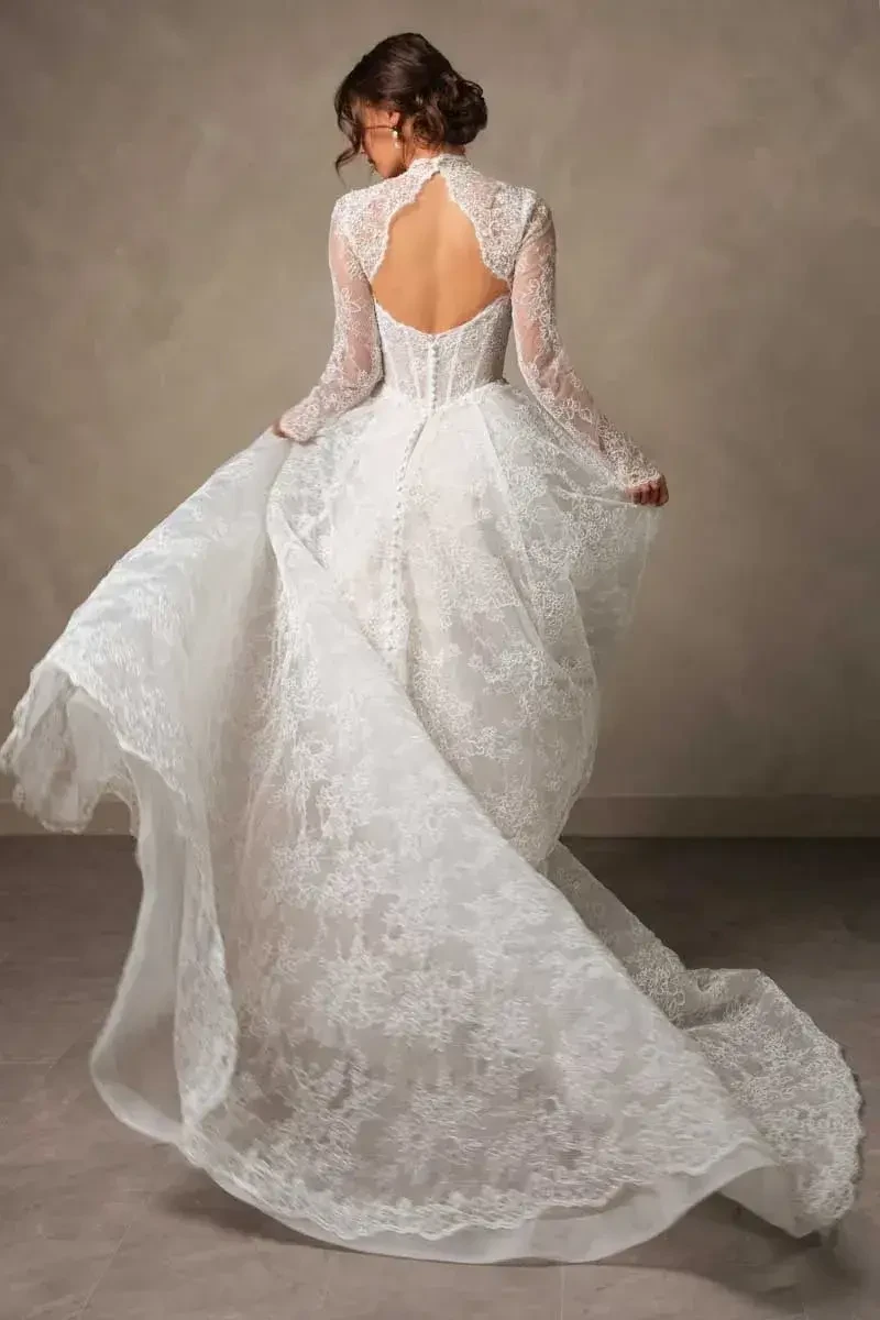 A woman wearing a white lace wedding dress, seen from the back, with long sleeves and a flowing train.