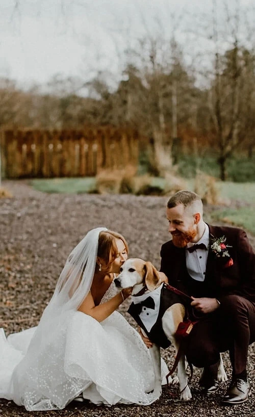 Сouple wearing a white gown and a black suit with a dog