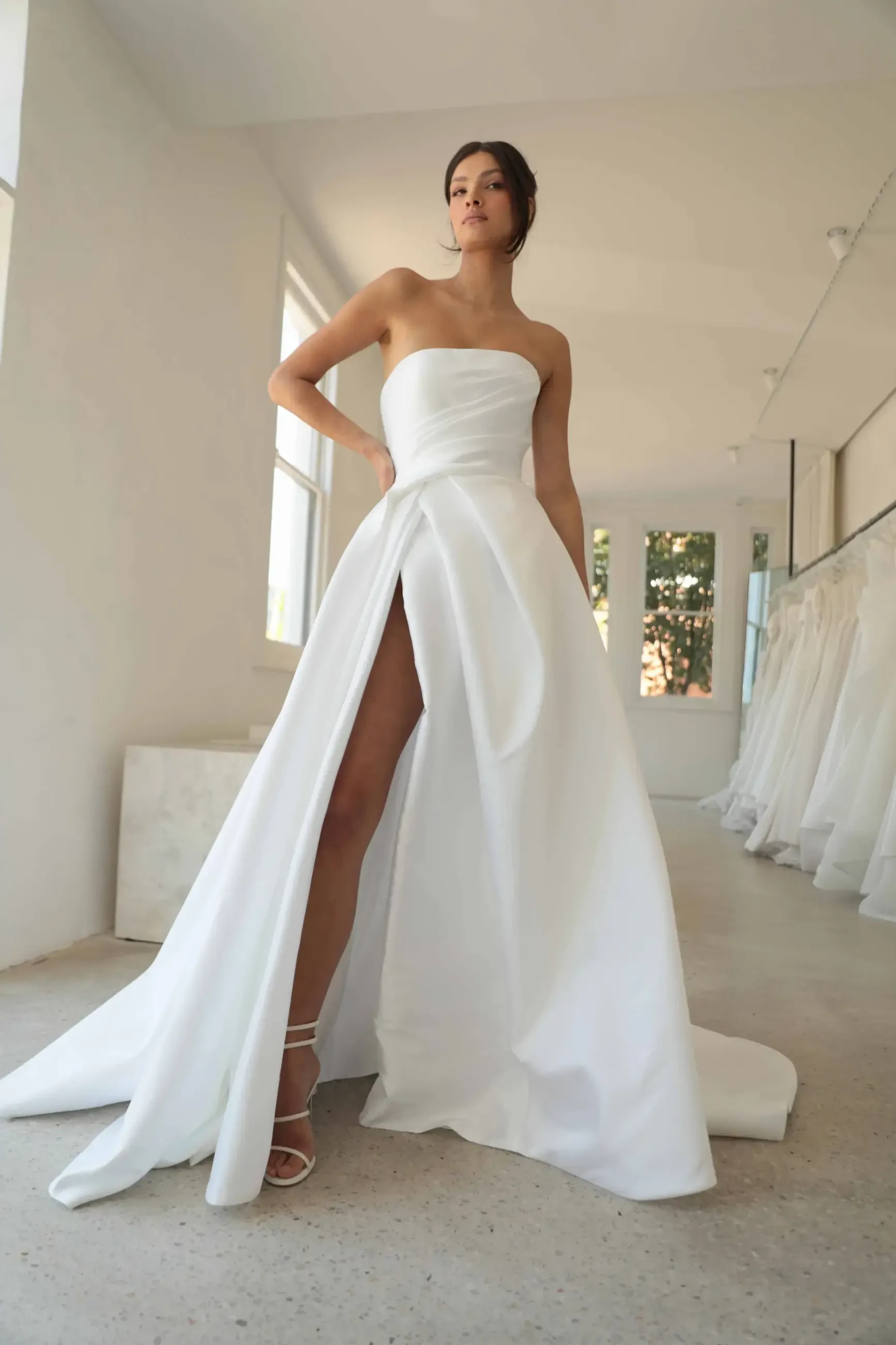 Model is wearing a strapless mikado gown with dramatic draping, a structured bodice, and a high front slit.